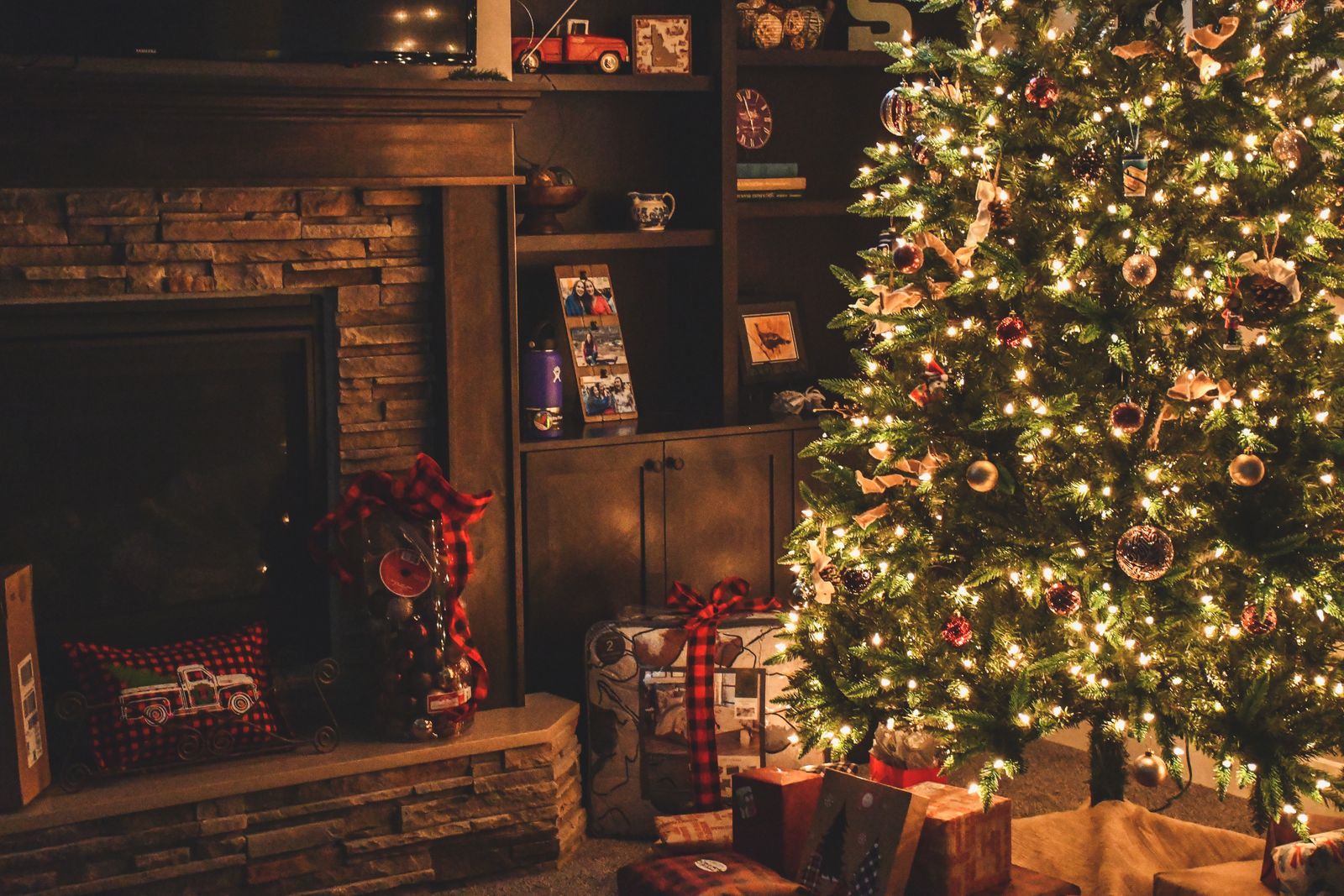 Wrapped gifts beneath a lit Christmas tree beside a stone fireplace