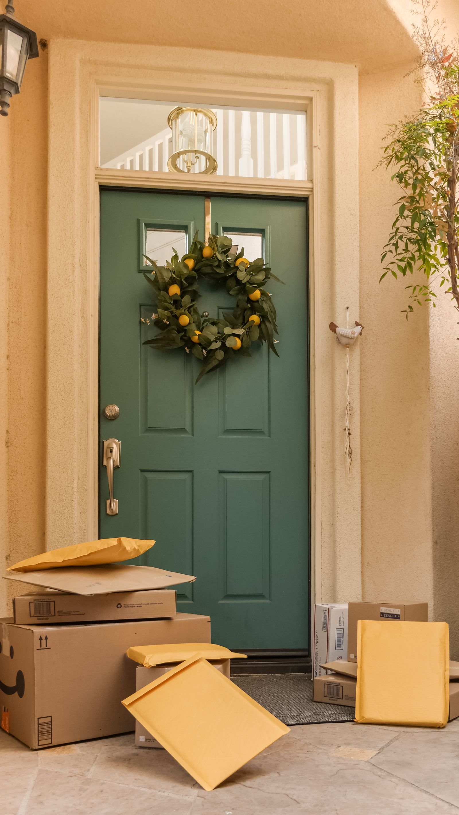 Parcels and mailers stacked at a green front door with a wreath