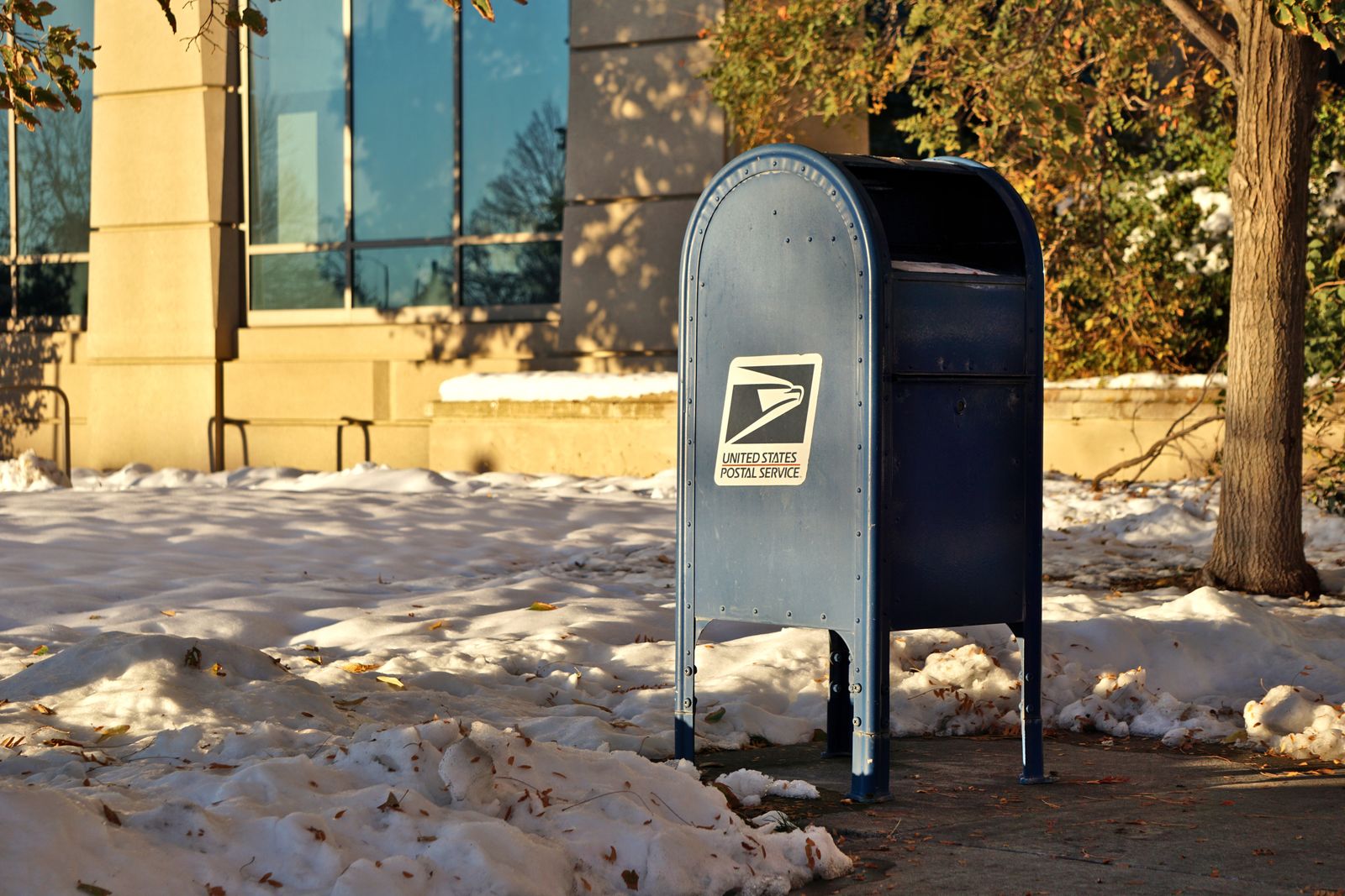 A USPS collection box standing in the snow in warm afternoon light