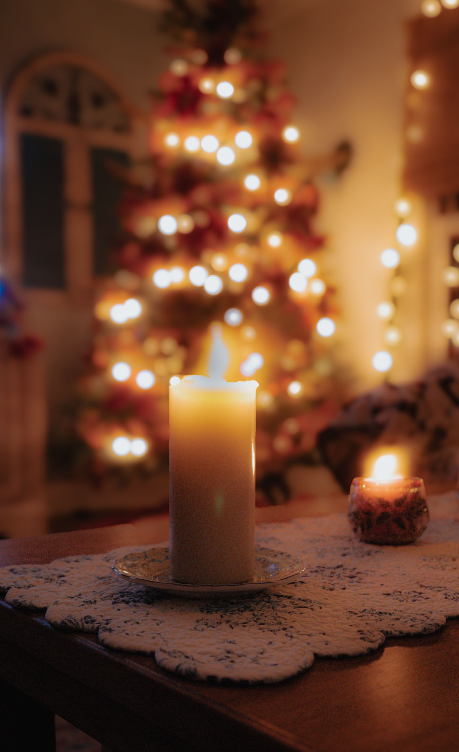 A lit candle in front of a softly glowing Christmas tree