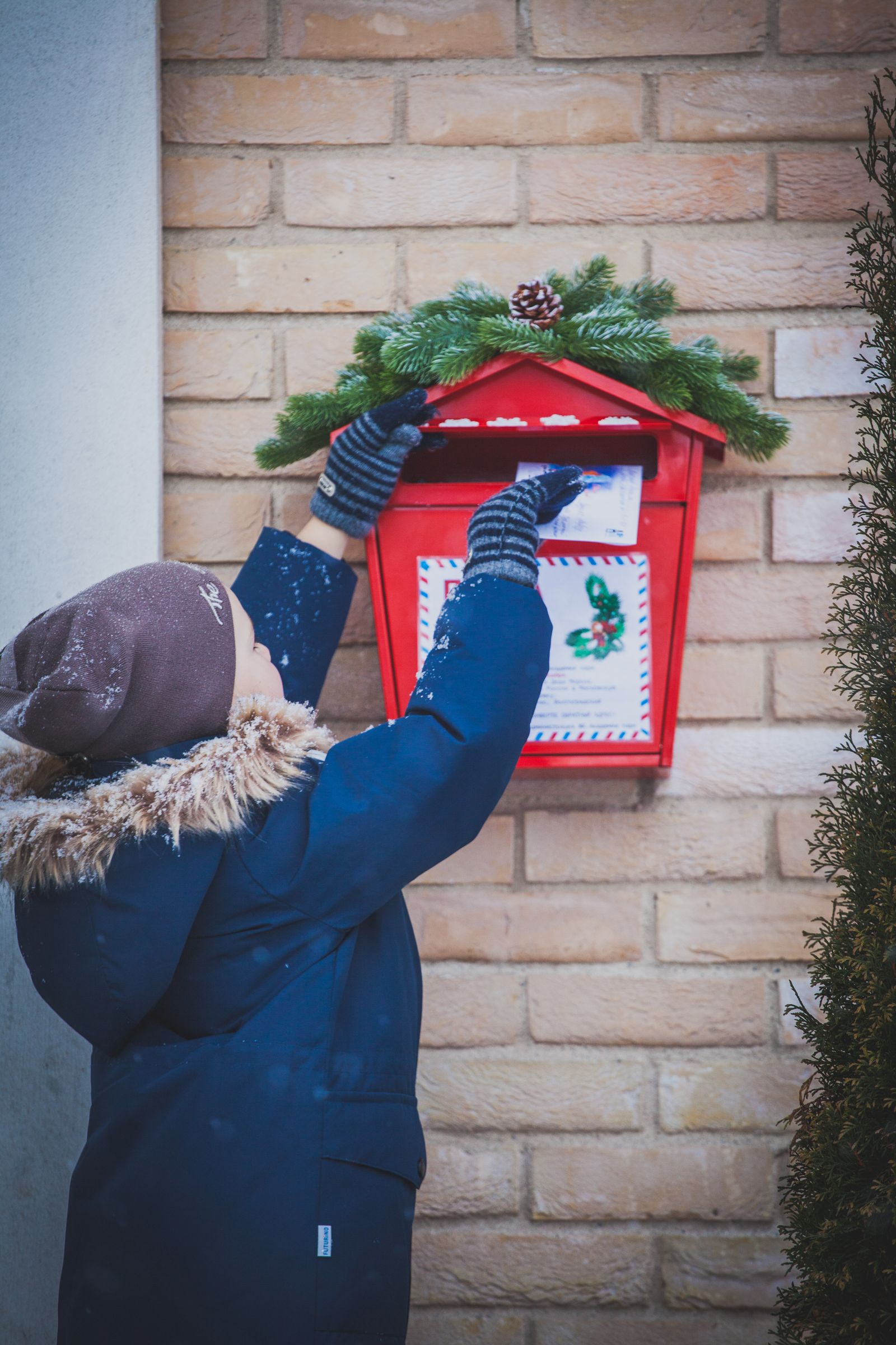 A child posting a letter into a garland-decked mailbox in the snow
