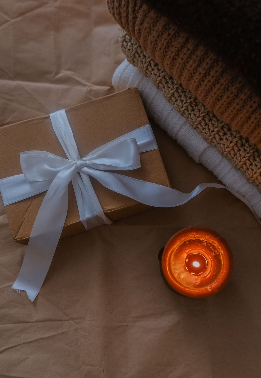 A gift box with folded knits and a glowing candle